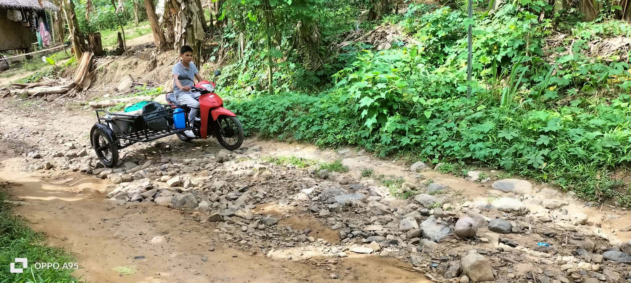 A motorcycle with sidecar crossing a rocky section of the community road