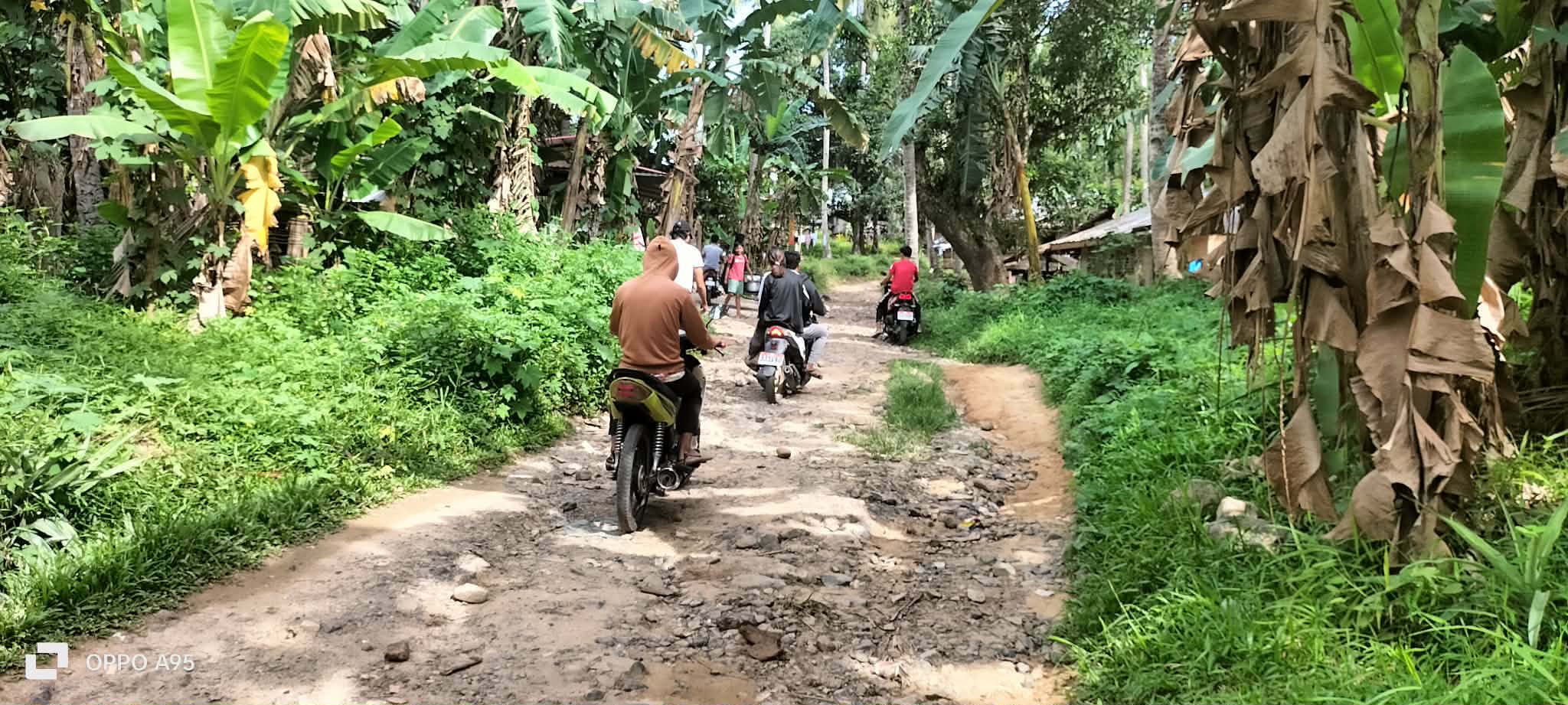 Motorcycles traveling along a rough community road bordered by greenery